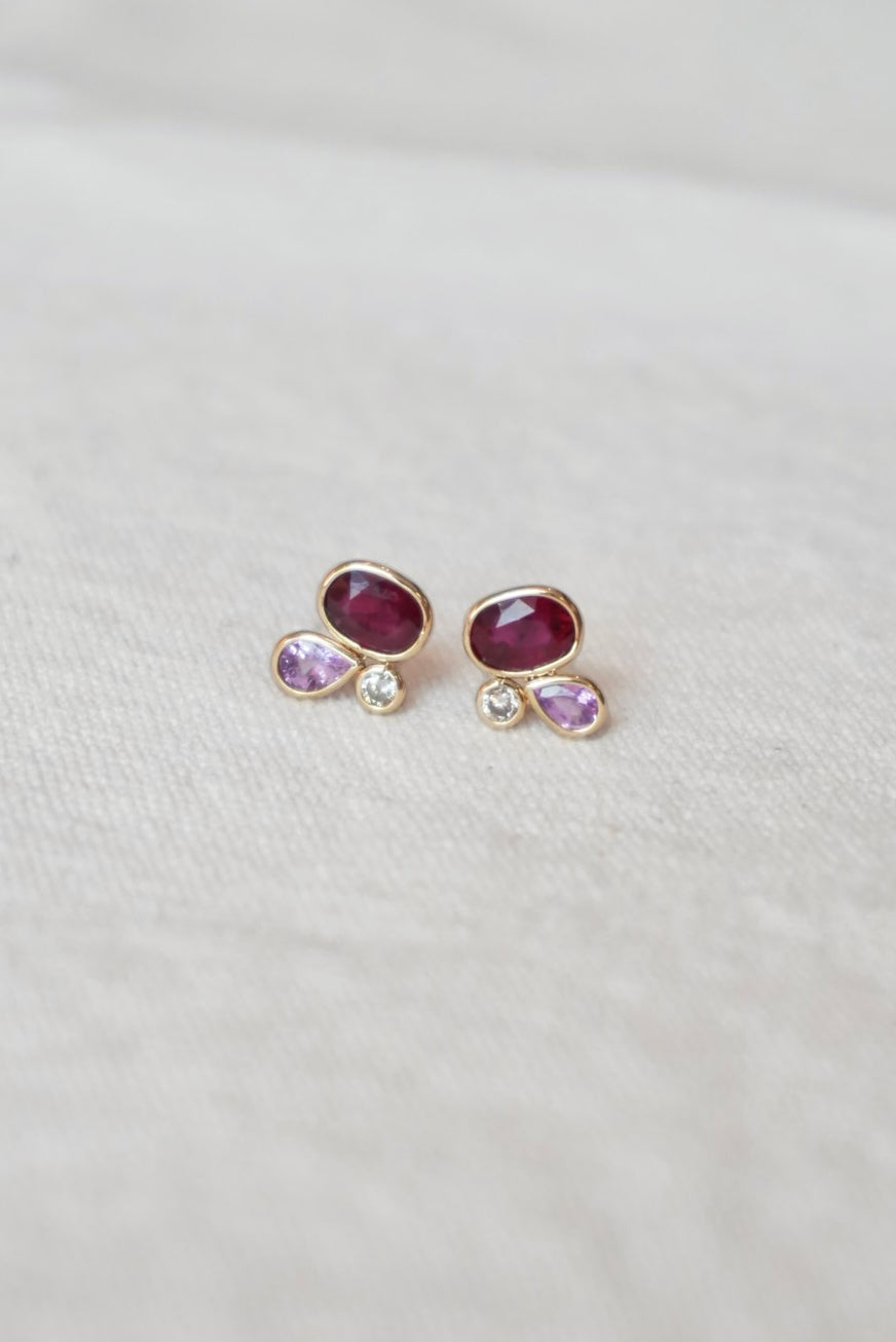 Pair of gold stud earrings with red and pink gemstones on a white background