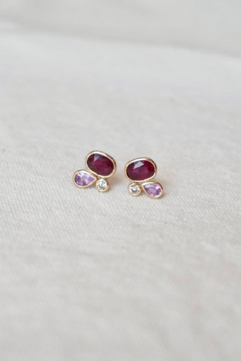 Pair of gold stud earrings with red and pink gemstones on a white background