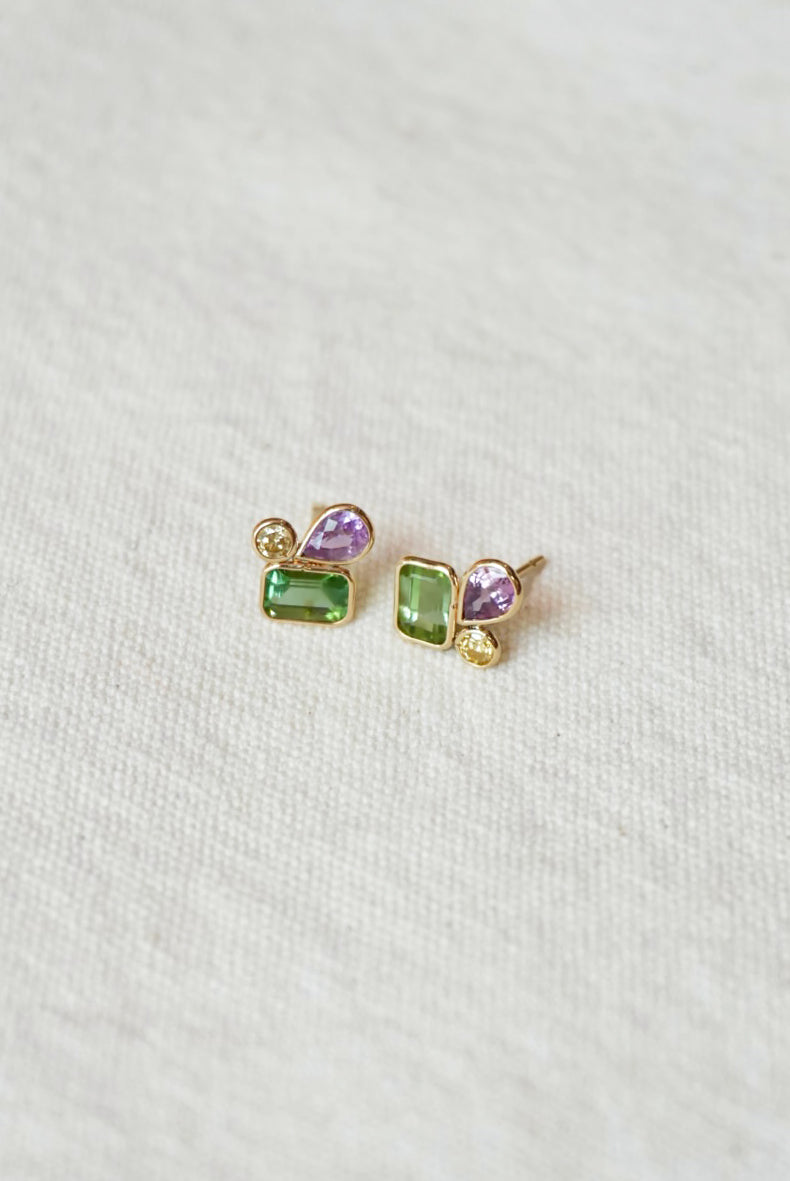 Pair of gold earrings with green and purple gemstones on a white background