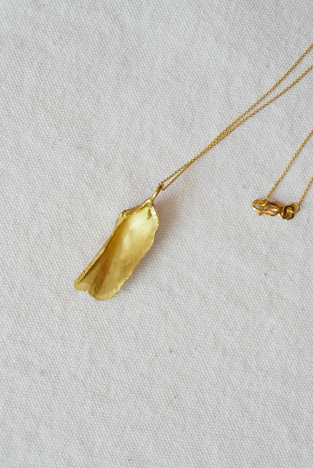 Gold shell pendant necklace on a light beige fabric background