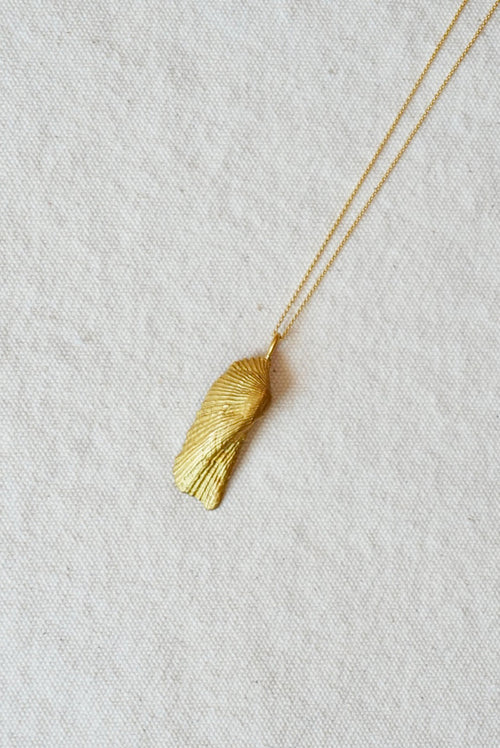 Gold necklace with a shell-shaped pendant on a light fabric background