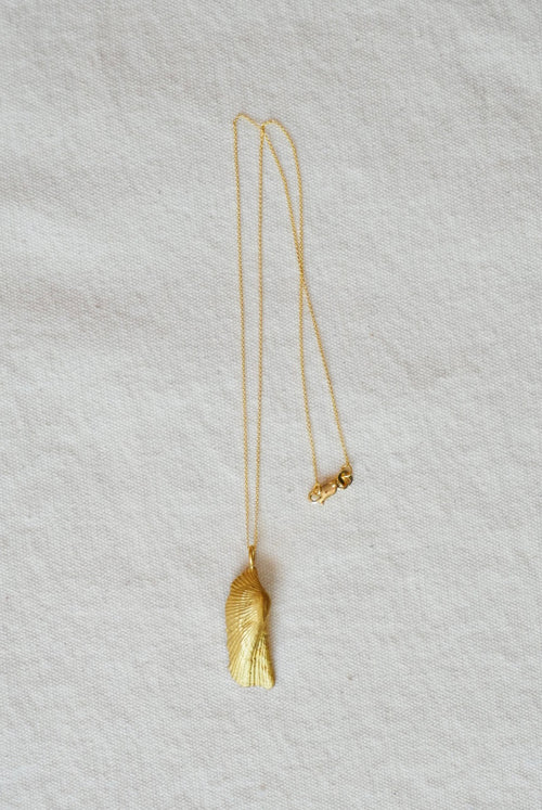 Gold necklace with a shell pendant on a light gray fabric background