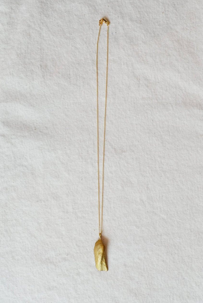 Gold necklace with a shell pendant on a light gray background