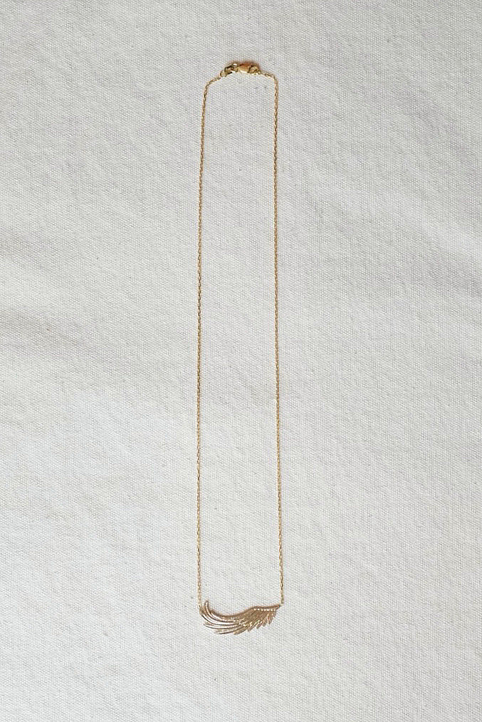 Gold necklace with wing pendent on a textured white surface