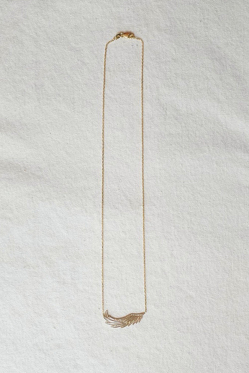 Gold necklace with wing pendent on a textured white surface