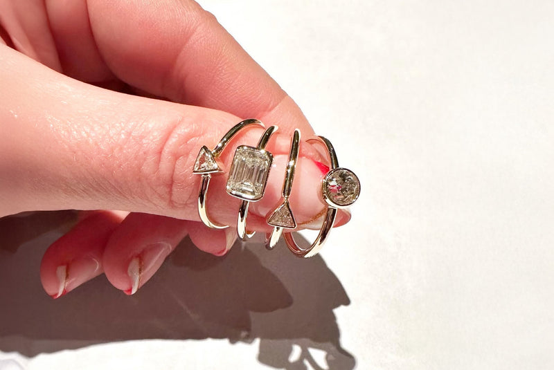 Hand wearing multiple gold rings on a light background