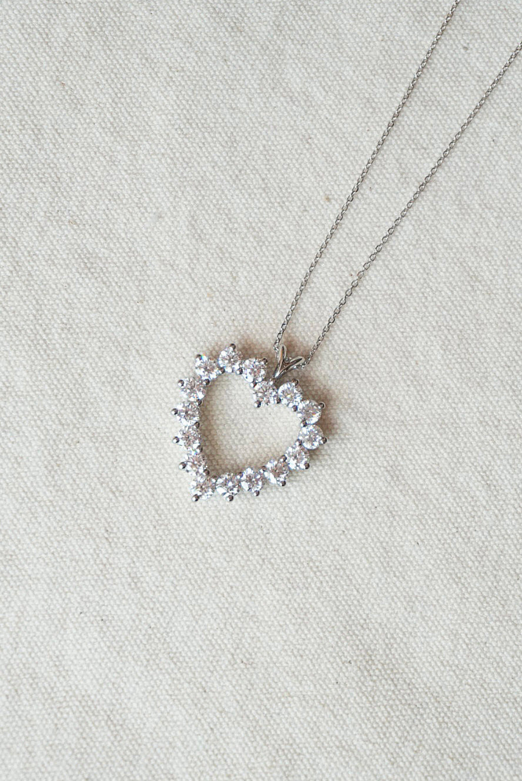 Heart-shaped necklace with small diamonds on a light cream fabric background