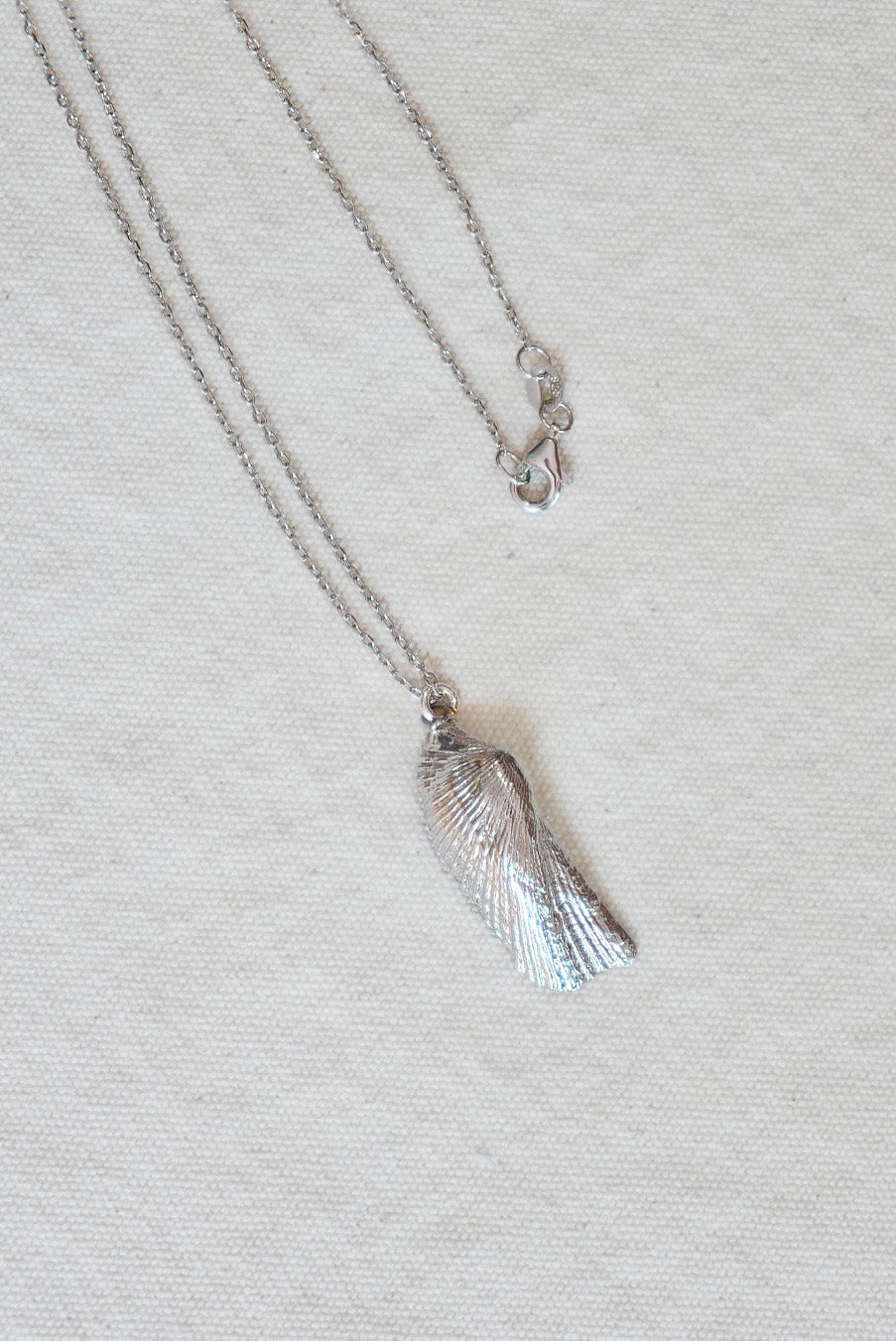 Silver shell necklace on a light gray fabric background