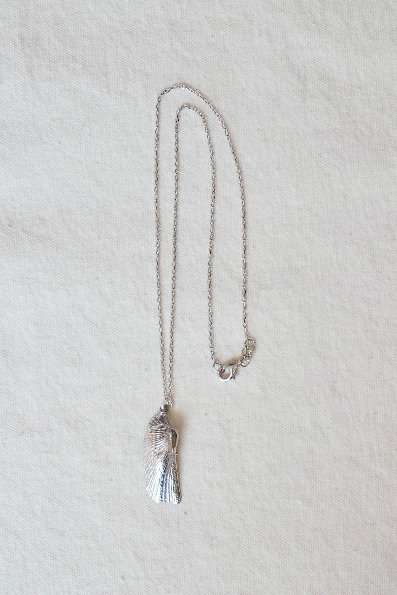 Silver necklace with a shell pendant on a light beige fabric background