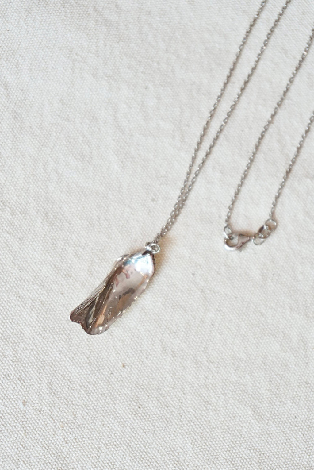 Silver necklace with a shell pendant on a light beige fabric background