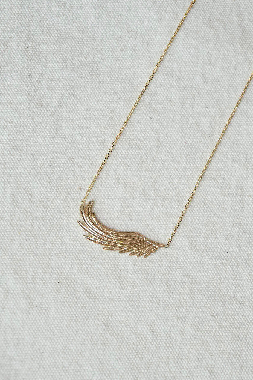 Gold necklace with a delicate wing pendant on a light gray fabric background