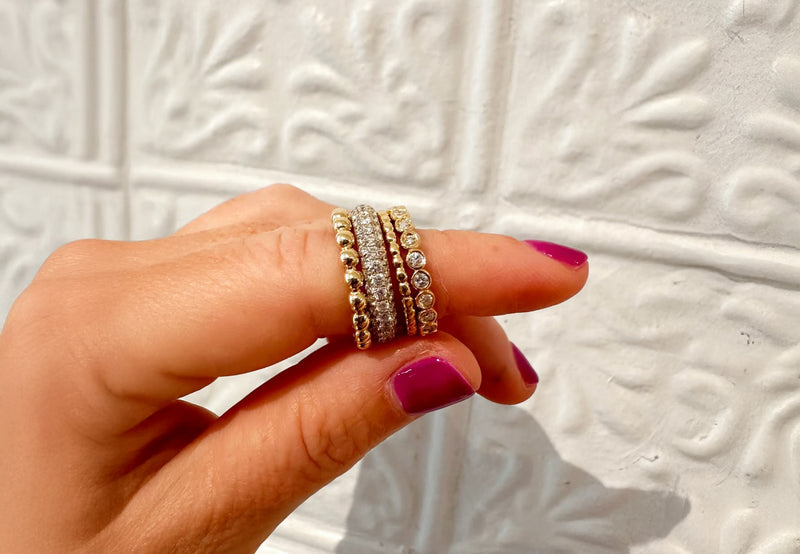 Finger holding multiple gold rings on a textured white background