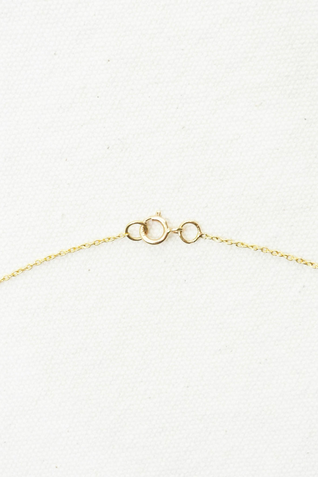 Close-up of a delicate gold chain necklace clasp on a textured white background.