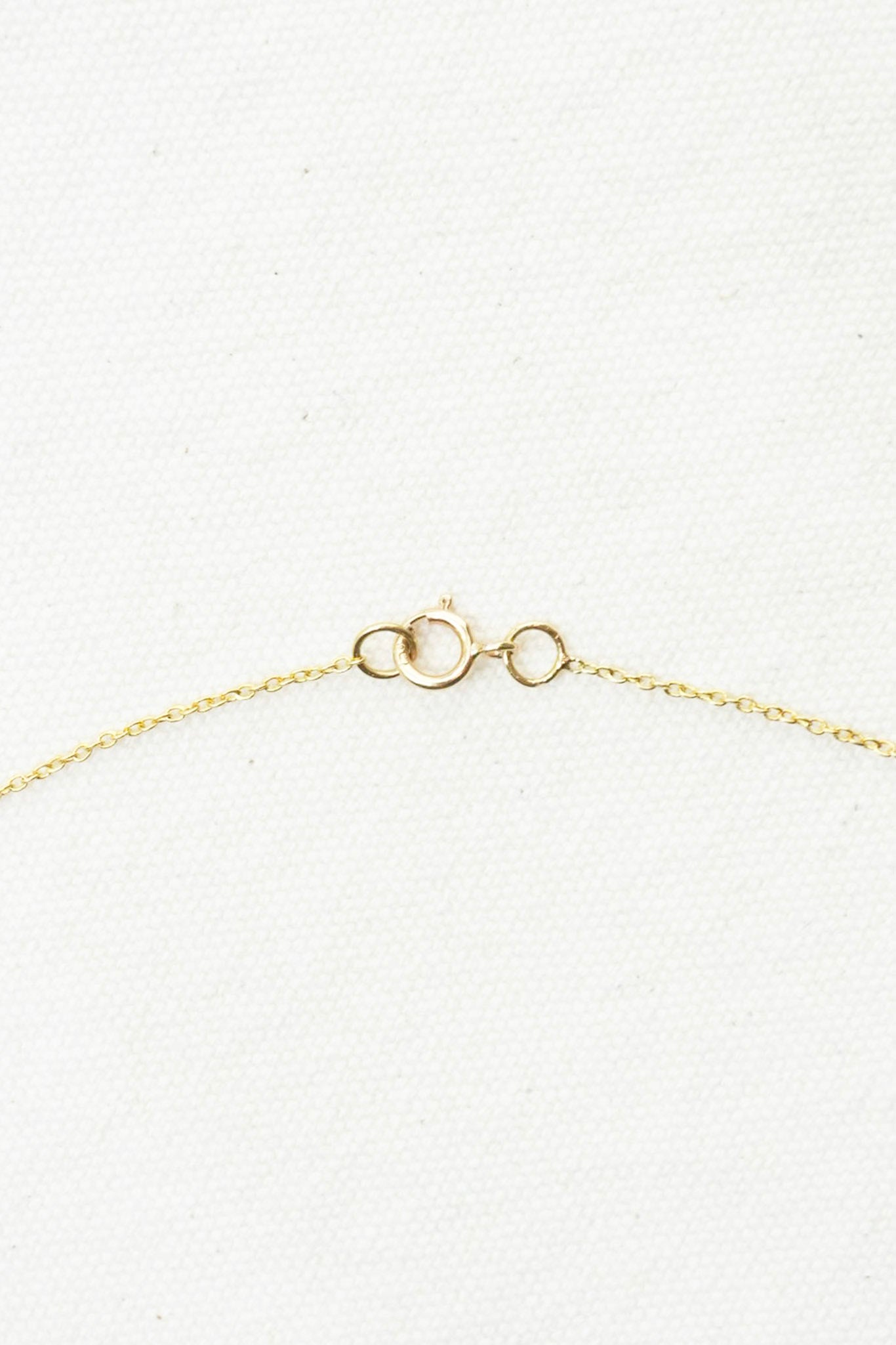 Close-up of a delicate gold chain necklace clasp on a textured white background.