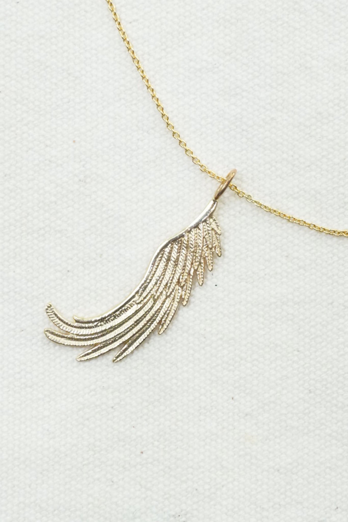A gold wing pendant necklace on a textured white background.