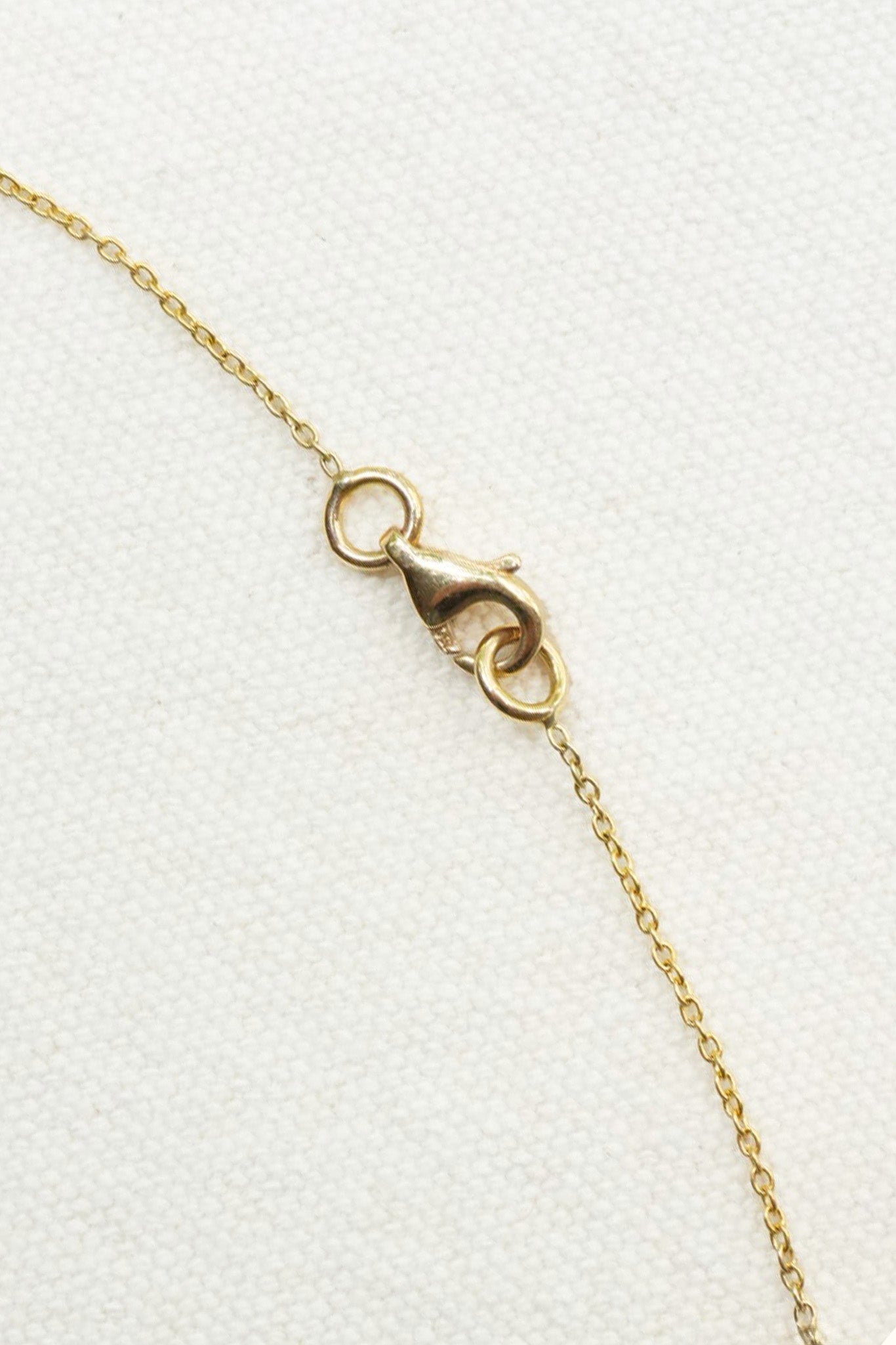 Close-up of a delicate gold chain necklace with a lobster clasp, laid diagonally on a textured white background.
