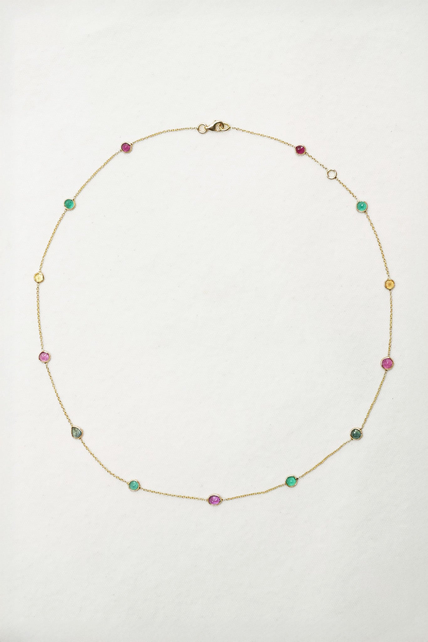 A delicate gold chain necklace with small, spaced multicolor gemstone beads, laid flat on a white background.
