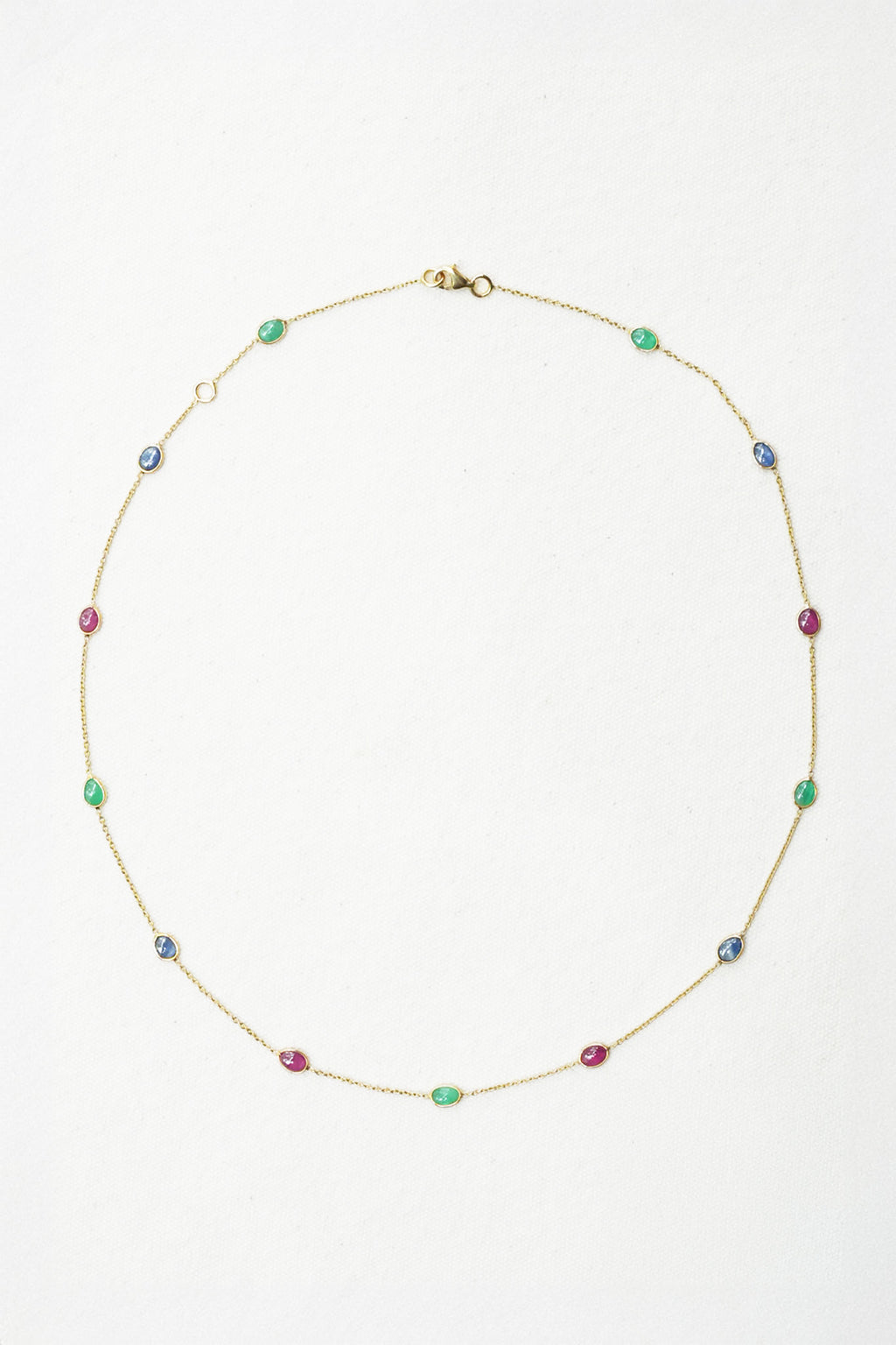 A delicate gold chain necklace featuring small, evenly spaced colorful gemstone beads in green, blue, and pink, displayed on a clean white background.
