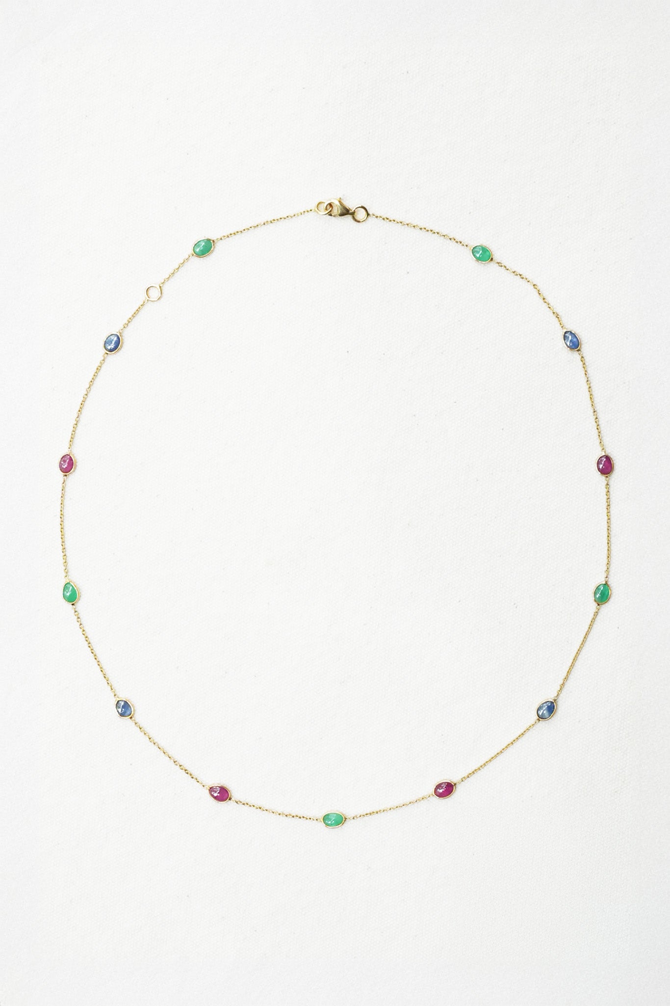 A delicate gold chain necklace featuring small, evenly spaced colorful gemstone beads in green, blue, and pink, displayed on a clean white background.